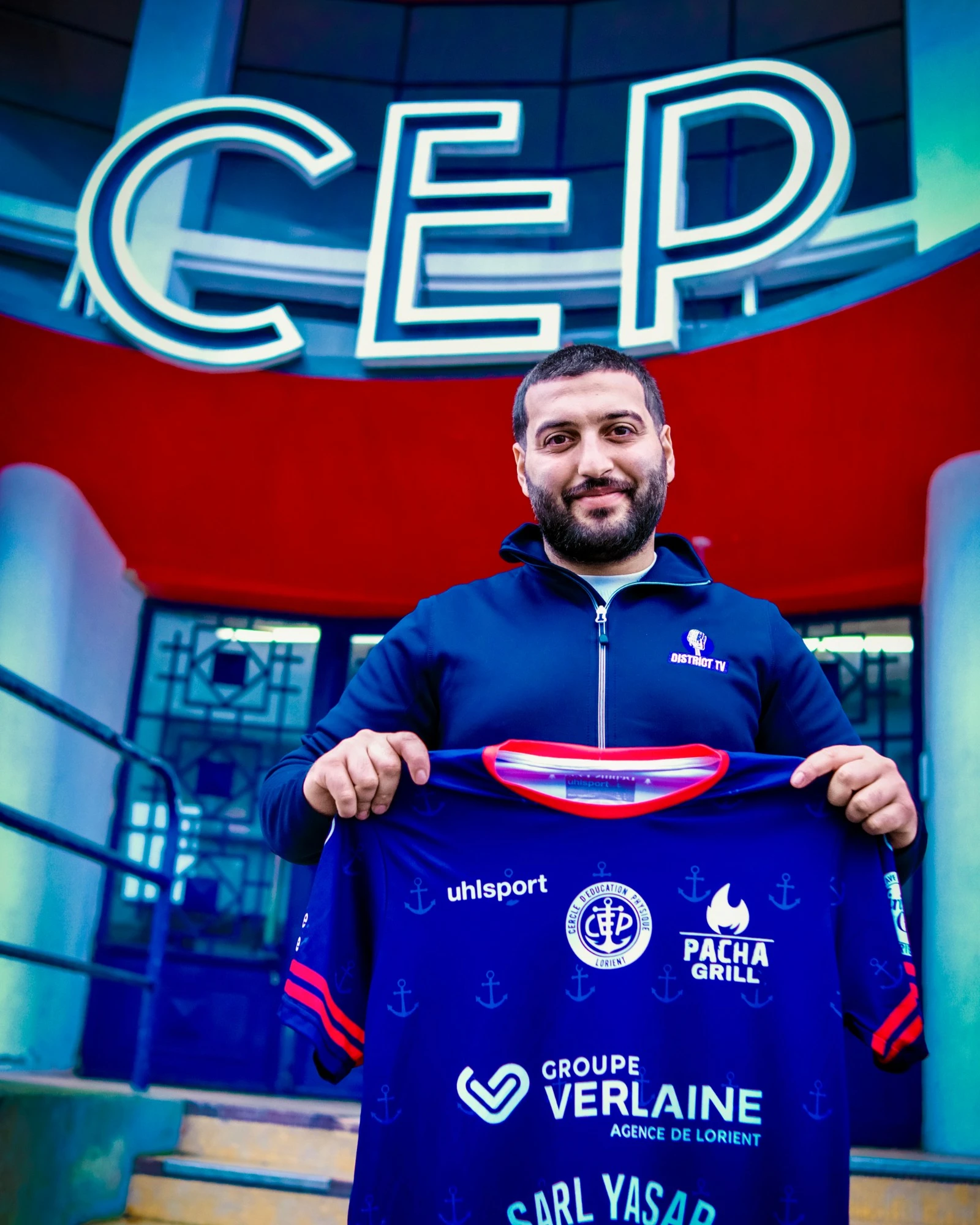 District TV au CEP Lorient : le maillot du club présenté devant l'entrée du siège